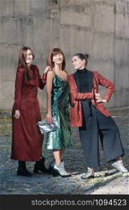 Street style Fashion portrait three charming women. Brown and green dress, Black, tile red jacket, silver shoes. Summer Spring Fall collection beautiful look. Togetherness, friendship, party concept