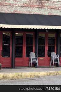 Street view of closed restaurant, gray chairs stacked by red front doors, band entrance on left side.