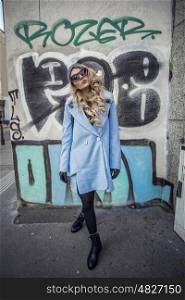 Streetstyle photo shoot of beautiful fashion blonde woman posing against graffiti wall