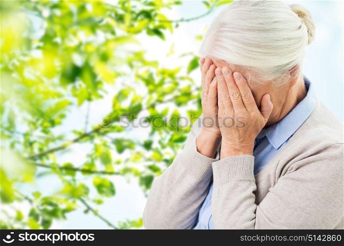 stress, age and people concept - senior woman suffering from headache or grief over green natural background. senior woman suffering from headache or grief
