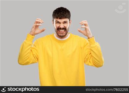 stress, emotions and people concept - angry young man in yellow sweatshirt over grey background. angry young man in yellow sweatshirt over grey