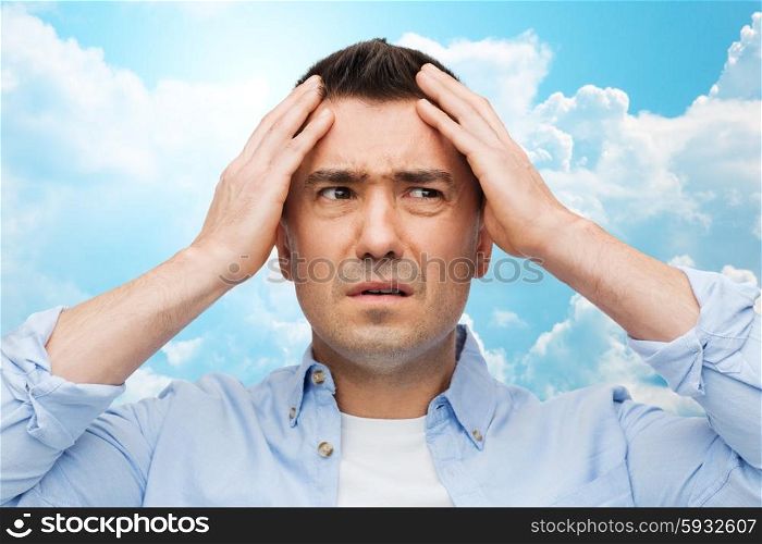 stress, headache, health care and people concept - unhappy man with closed eyes touching his forehead over blue sky and clouds background