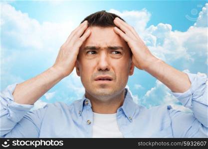 stress, headache, health care and people concept - unhappy man with closed eyes touching his forehead over blue sky and clouds background