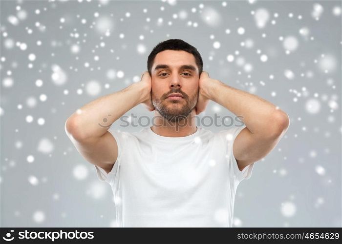 stress, hearing problem, winter, christmas and people concept - latin man covering his ears with hand palms over snow on gray background