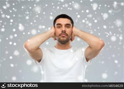 stress, hearing problem, winter, christmas and people concept - latin man covering his ears with hand palms over snow on gray background