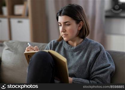 stress, mental health and depression concept - sad crying woman with diary sitting on sofa at home. crying woman with diary sitting on sofa at home