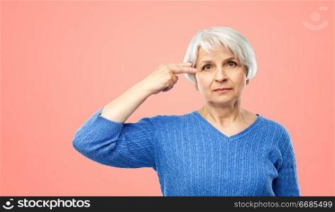 stress, mental health and old people concept - portrait of senior woman in blue sweater making finger gun gesture over pink or living coral background. senior woman making finger gun gesture