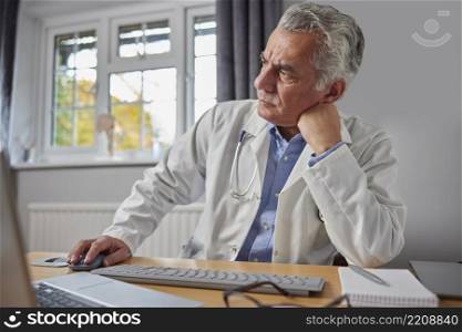 Stressed And Overworked Doctor In White Coat At Desk In Office