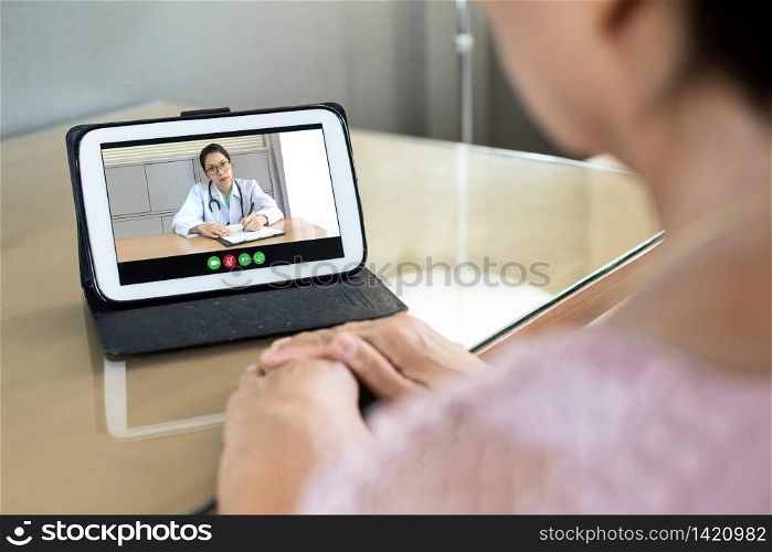 Stressed Asian Senior woman talking and consulting with Female Doctor about her symptoms from Coronavirus via internet and wireless technology. Rear view of old female making video call from home with physician via digital tablet during quarantine.