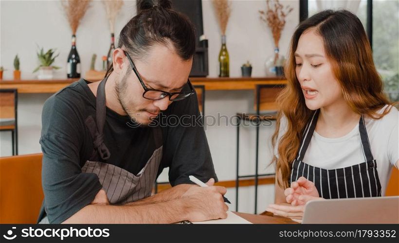 Stressed Asian small business owners couple using laptop discussing project and finance with documents of shop for the month at cafe. Woman and man doing paperwork together, paying taxes online.