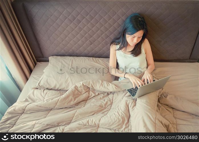 Stressed Asian woman using a laptop on bed in bedroom