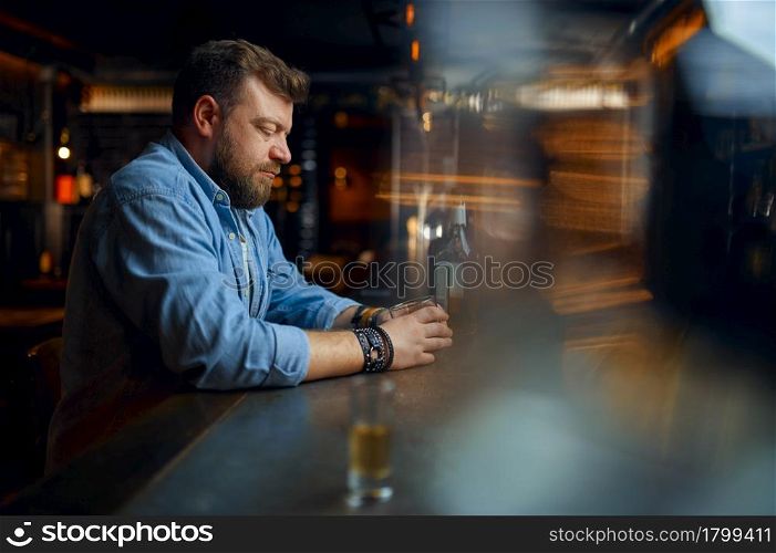 Stressed bearded man drinks alcohol at the counter in bar. One male person resting in pub, human emotions and leisure activities, depression, stress relief. Stressed man drinks alcohol at the counter in bar
