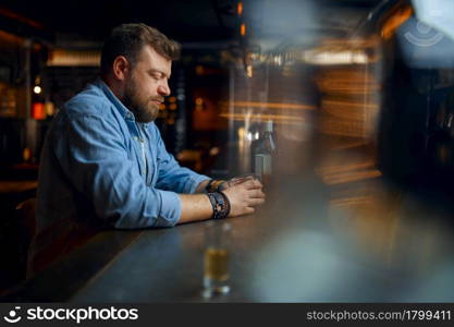 Stressed bearded man drinks alcohol at the counter in bar. One male person resting in pub, human emotions and leisure activities, depression, stress relief. Stressed man drinks alcohol at the counter in bar