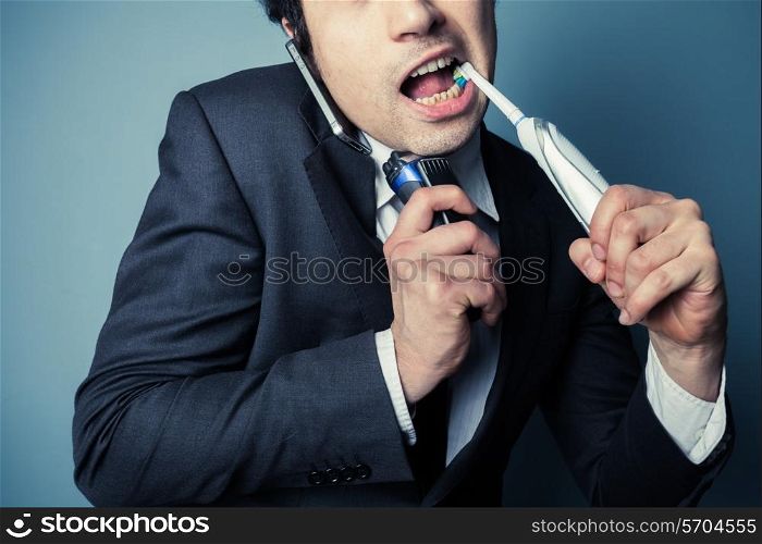 Stressed businessman is on the phone while brushing his teeth and shaving to save time