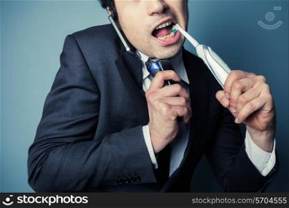Stressed businessman is on the phone while brushing his teeth and shaving to save time