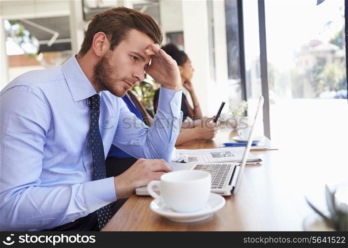 Stressed Businessman Using Laptop In Coffee Shop