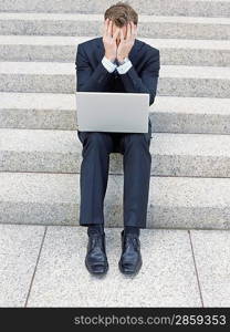 Stressed businessman using laptop on steps