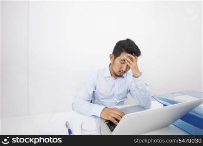 Stressed businessman with laptop sitting at desk in office