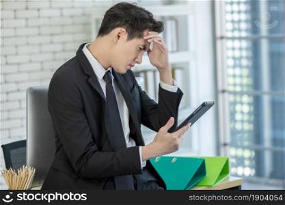 Stressed businessman worked with a tablet and having a headache after business losses In the office room background.