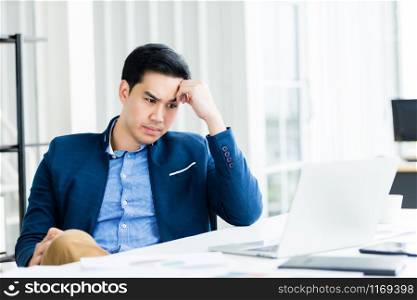 Stressed businessman worked with laptop computer and having a headache after business losses In the office room background.