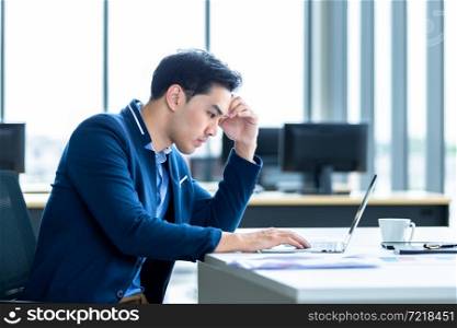 Stressed businessman worked with laptop computer and having a headache after business losses In the office room background.