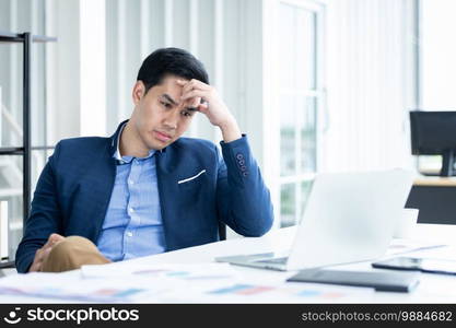 Stressed businessman worked with laptop computer and having a headache after business losses In the office room background.