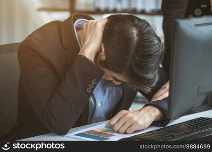 Stressed businessman worked with laptop computer and having a headache after business losses In the office room background.