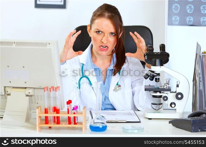 Stressed female doctor sitting at office table and holding hands near head&#xA;