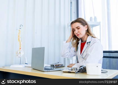 Stressed female doctor with stethoscope have headache working with laptop computer on wooden table in Hospital background