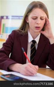 Stressed Female Pupil In Uniform Sitting School Exam