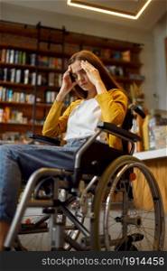 Stressed female student in wheelchair, disability, bookshelf and university library interior on background. Disabled young woman studying in college, handicapped or paralyzed people get knowledge. Stressed female student in wheelchair, disability