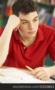 Stressed Male Teenage Student Studying In Classroom
