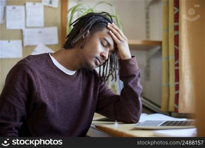 Stressed Male University Or College Student With Poor Mental Health Studying With Laptop At Desk In Room