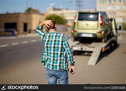 Stressed man having problems with car. Driver looking after tow truck taking away his automobile. Stressed man having problems with his car