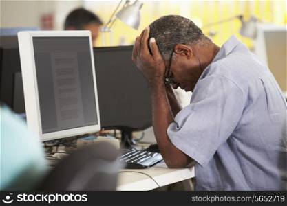 Stressed Man Working At Desk In Busy Creative Office