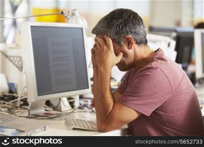 Stressed Man Working At Desk In Busy Creative Office