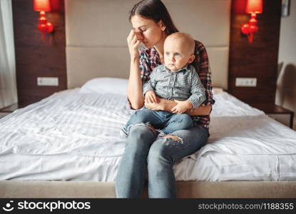 Stressed mother with little child sitting on the bed, motherhood problems. Depressed mom and son together at home, parenthood trouble