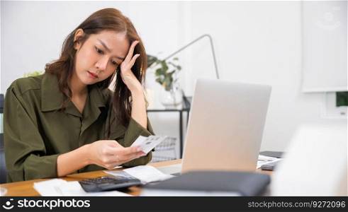 Stressed over bills. Asian young woman with laptop holding papers in her hands she calculating dealing financial budget on desk, female worried have stress headache after calculate cost, money problem