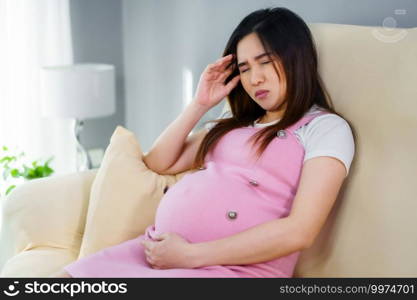 stressed pregnant woman has a headache on sofa in the living room