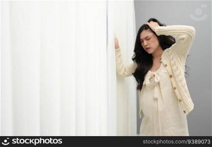 stressed pregnant woman suffering headache near the window 