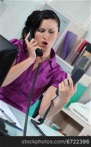 Stressed secretary answering two telephones
