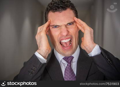 Stressed, shouting, screaming, depressed angry businessman holding his head in pain and anger from stressful migraine headache or mental health crisis