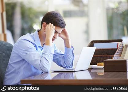 Stressed Teenage Boy Using Laptop On Desk At Home