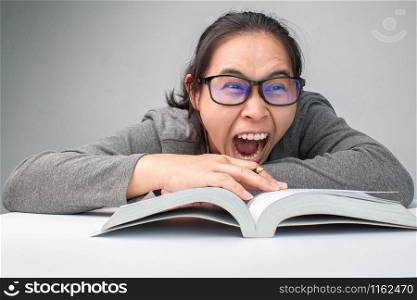 Stressed woman reading a book to exam and yelling on grey background.
