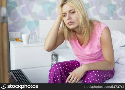 Stressed woman suffering from headache sitting on bed at home