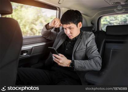 stressed young business man using a smartphone while sitting in the back seat of car