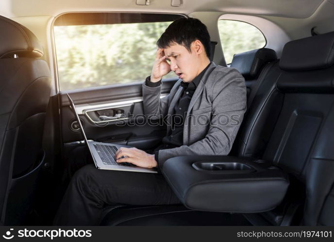 stressed young business man using laptop computer while sitting in the back seat of car