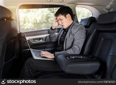 stressed young business man using laptop computer while sitting in the back seat of car