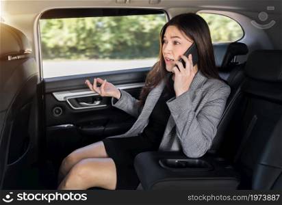 stressed young business woman talking problem on a mobile phone while sitting in the back seat of car