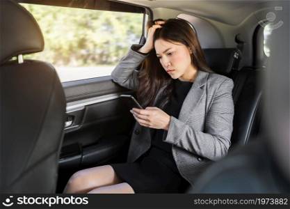 stressed young business woman using a smartphone while sitting in the back seat of car